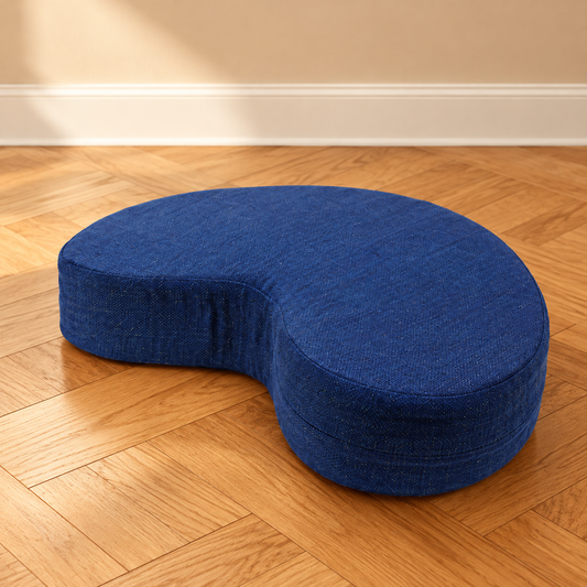 Crescent meditation cushion in Royal Blue on a warm wooden floor; AI-assisted background styling.