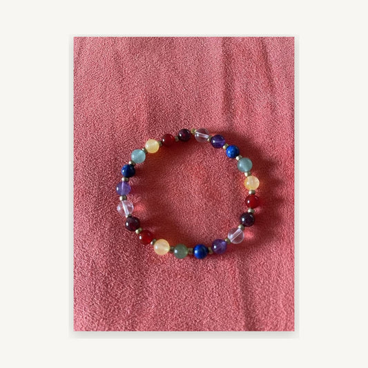 Actual seven-chakra gemstone stretch bracelet with gold-toned spacer beads on neutral ivory mat