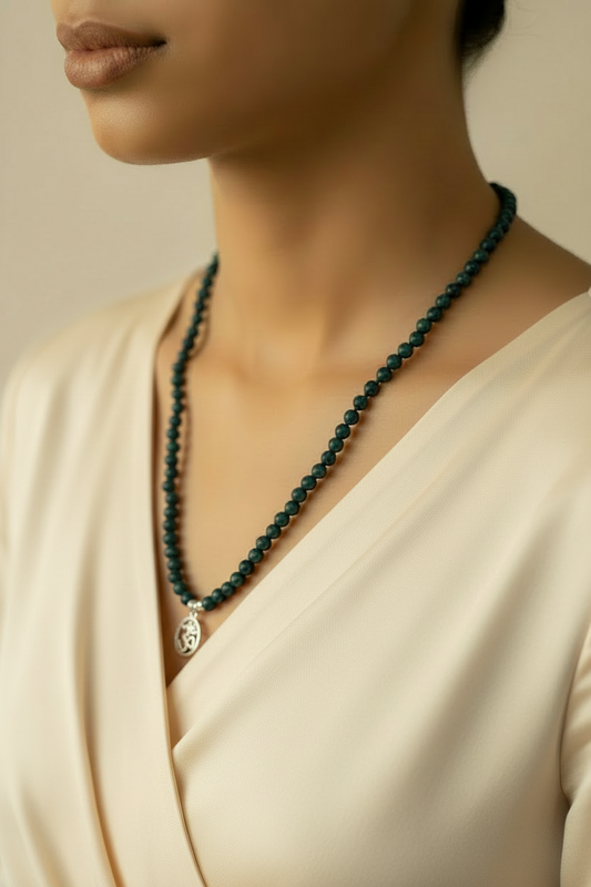 Person wearing a dark green beaded necklace with a silver pendant on a neutral background